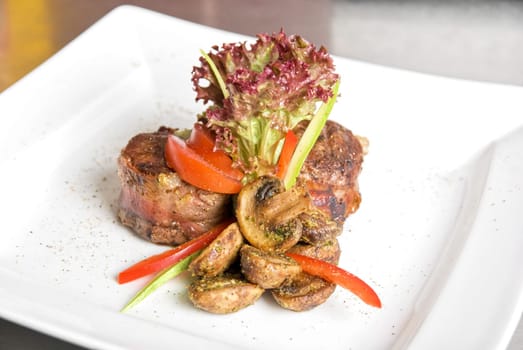 Tasty beef steak grilled in a cast-iron ribbed fry pan with bacon decorated with vegetables and roasted mushrooms