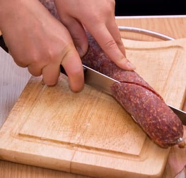 Hand closeup cuts salami with slice pieces at table