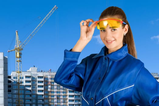 Builder pretty girl at safety glasses on a building background