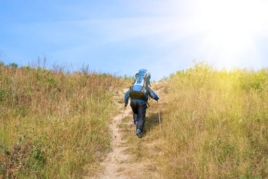 Hiker with rucksack up-hill at summer sunny day