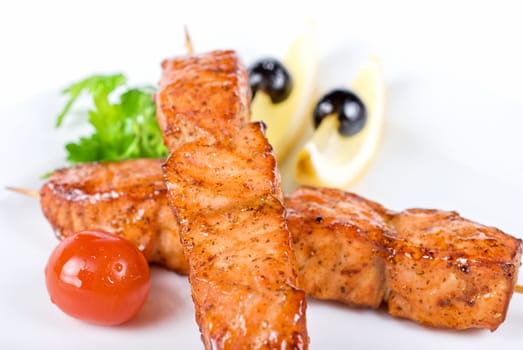 salmon kebab at plate with green lettuce and lemon on a white