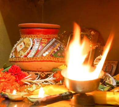 square format portrait of Hindu Hinduism religion religious worship of Navratri event home with puja decorated clay pot matti, flowers a ghee diwa candle and pictures of hindu idols crop margin