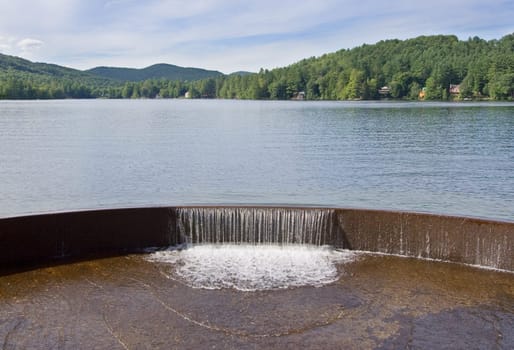 A lake in the mountains with a waterfall over a dam in the foreground