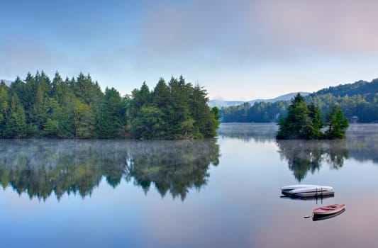 A lake in the early morning with fog on the water. A boat and dock are in the foreground.