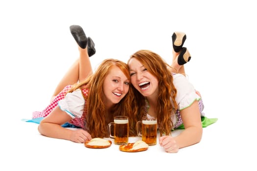 Two happy women in dirndl with beer and pretzels lying on the floor on white background