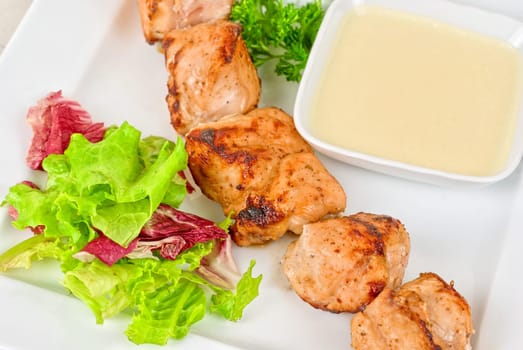 Grilled chicken kebab with sauce and greens on white plate
