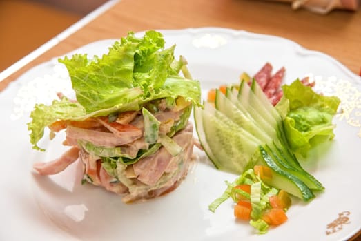 Salad from different kinds of sausages, cucumbers, peppers, lettuce with sour cream sauce