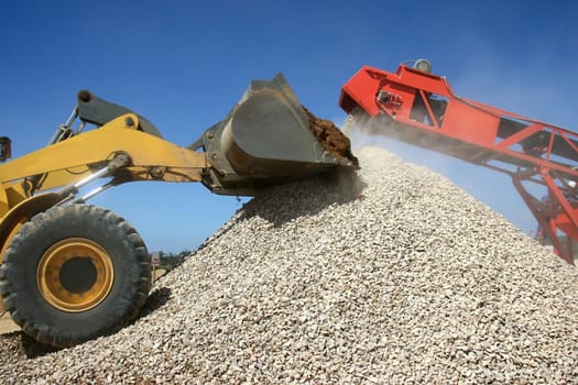 Front end loader and conveyor belt on a pile of graded stone