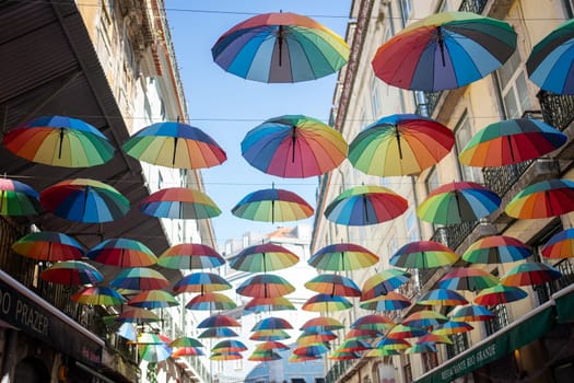 From below shot of rainbow umbrellas hanging in city during pride parade. Multicolored objects are decorated amidst buildings during daytime