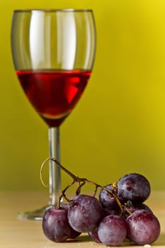 Grapes with red wine and a bottle of wine with yellow background