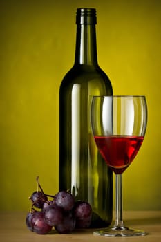 Grapes with red wine and a bottle of wine with yellow background