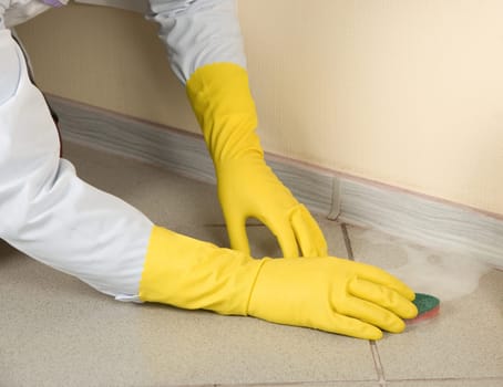 Hands in yellow gloves with sponge, washing floor and plinth