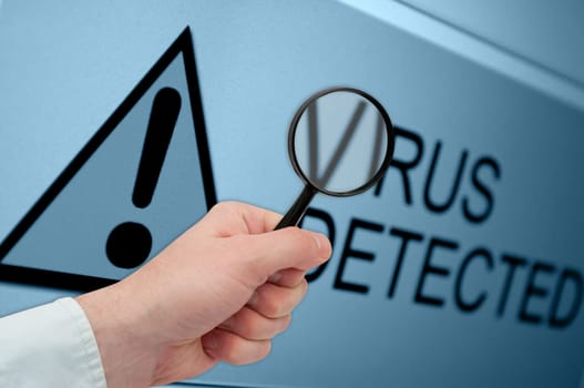 Man&#039 s Hand Holding Magnifying Glass over Virus Detected Sign on Monitor