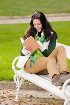 Autumn park young woman reading book sitting on the bench
