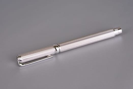 Stylish ballpoint pen of white gold on a grey