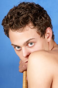 Portrait of a sexy shirtless young man with blue eyes and brown hair over a blue background