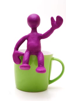 Purple man puppet of plasticine sitting on cup