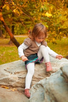 Small girl (3 years) tying shoelace in the autumn park at the evening