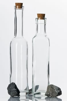 Empty glass bottles with corks and stones on white background