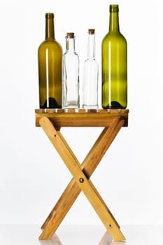 Empty glass bottles on wooden stool against white background