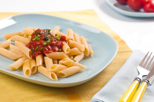 Pasta with tomato sauce and fresh chives on blue dishes