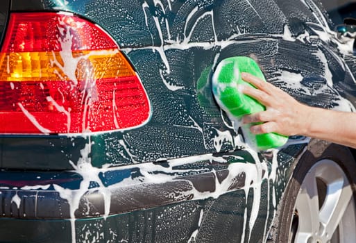Closeup image of a hand with a soapy sponge washing a vehicle