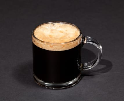 Black expresso coffee with heady froth in a glass mug or cup