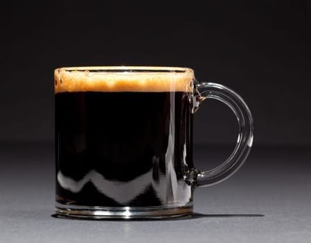 Black expresso coffee with heady froth in a glass mug or cup