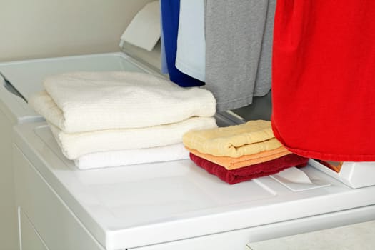Piles of bath and hand towels folded on top of a dryer and washer along with five shirts hung up ready for storage.
