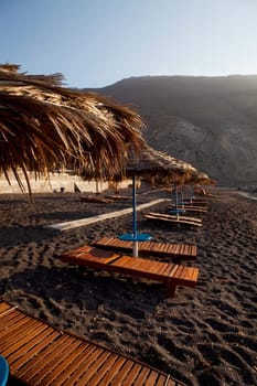 Beach umbrellas and sunbeds at sunrise in Perissa beach, Santorini, Greece