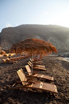 Beach umbrellas and sunbeds at sunrise in Perissa beach, Santorini, Greece