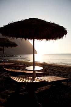 Beach umbrellas and sunbeds at sunrise in Perissa beach, Santorini, Greece