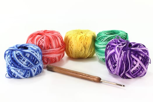 Colorful ball of wool and crochet hook against white background