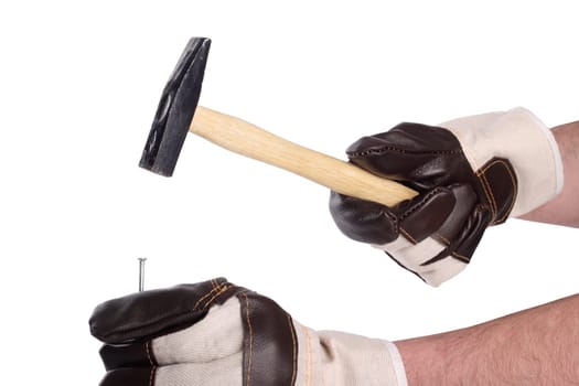 Hands with work gloves hammer in a nail with a hammer.