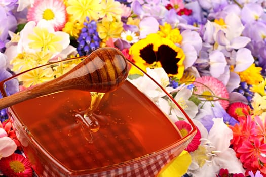 Glass bowl with honey and measuring spoon in flowers