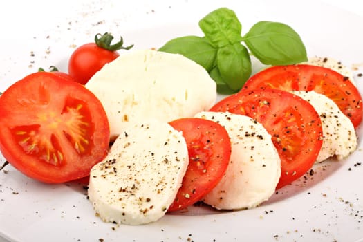 Mozzarella and tomato slices on plates with pepper and basil.