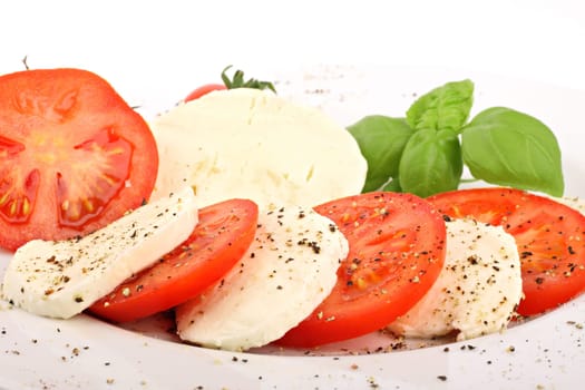 Mozzarella and tomato slices on plates with pepper and basil.