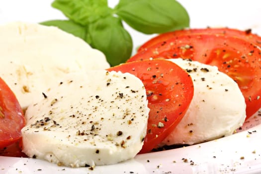Mozzarella and tomato slices on plates with pepper and basil.