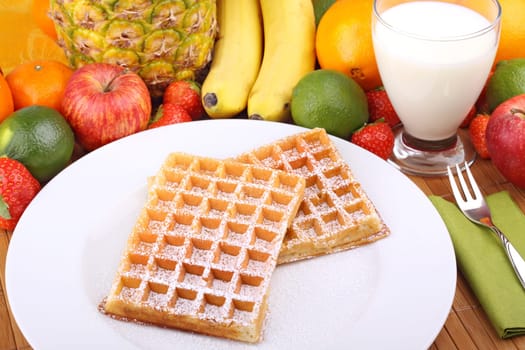 Waffle with powdered sugar on white plate in front of fruits.