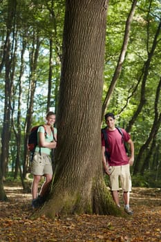 young man and woman during hiking excursion, posing near large tree and smiling. Vertical shape, front view, full length