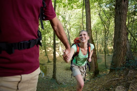 young man and woman walking in woods, with man helping his girlfriend. Horizontal shape, three quarter length