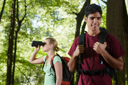 young people trekking among trees and looking at birds with binoculars. Horizontal shape, side view, waist up