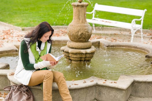 Autumn park young woman reading book sitting on fountain
