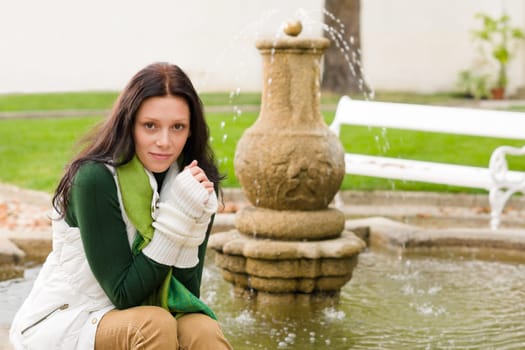 Autumn park young beautiful woman sitting on fountain cloudy day