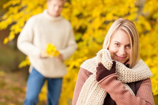 Autumn happy young woman in park with man in background