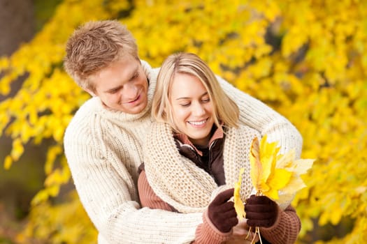 Young playful couple happy picking leaves in autumn park outfit