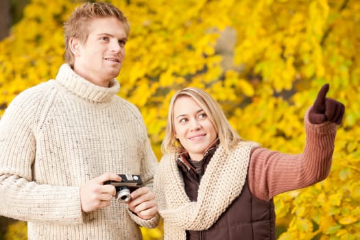 Young happy couple making photo in autumn park pointing at