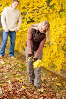 Young happy couple picking leaves in autumn park playful