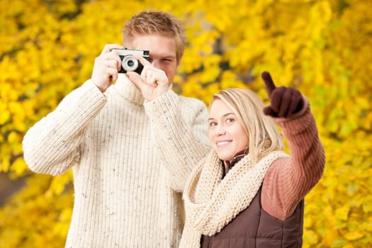 Young happy couple making photo in autumn park pointing at