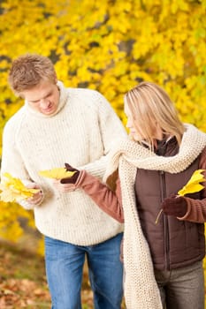Young couple picking leaves in autumn park outfit
